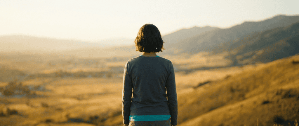 Confiance en soi : Jeune silhouette de dos au sommet d'une colline face au soleil levant