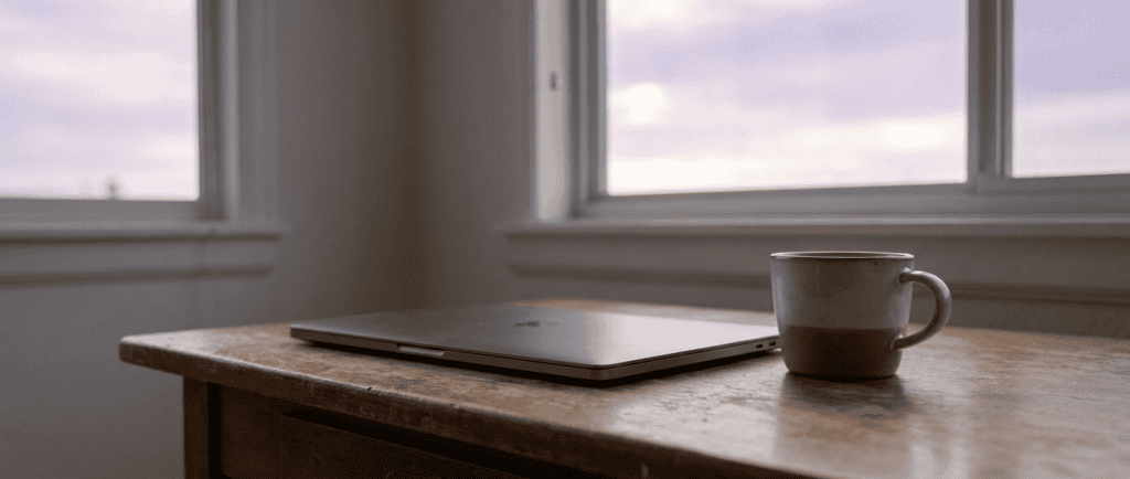 Burn-out entrepreneurial : Ordinateur portable fermé sur un bureau, tasse de café, aube naissante par la fenêtre