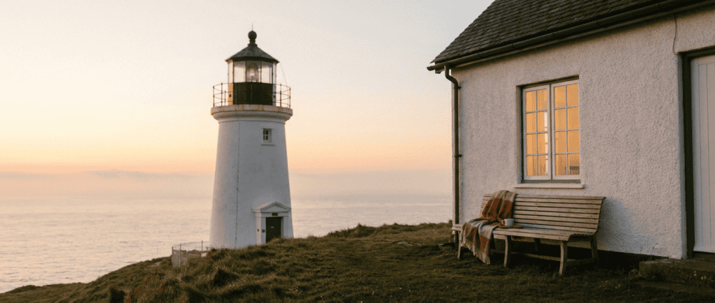 Anxiété généralisée : Phare au petit matin face à une mer calme, brume qui se dissipe dans une lumière orangée