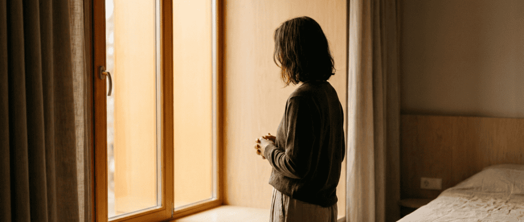 Personne contemplative près d'une fenêtre dans une lumière chaude, à un moment de décision — illustration de l'article sur l'auto-sabotage.